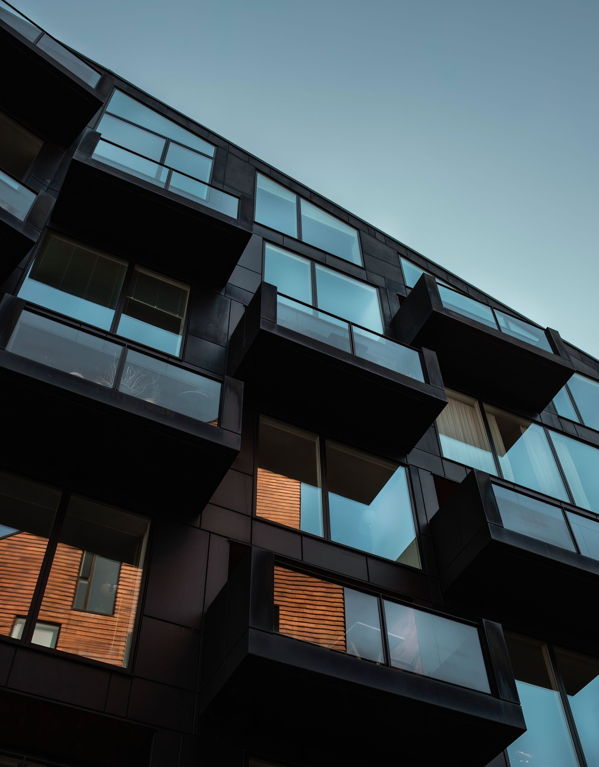 Low angle view of modern residential building facade in Copenhagen, showcasing glass balconies and reflections.